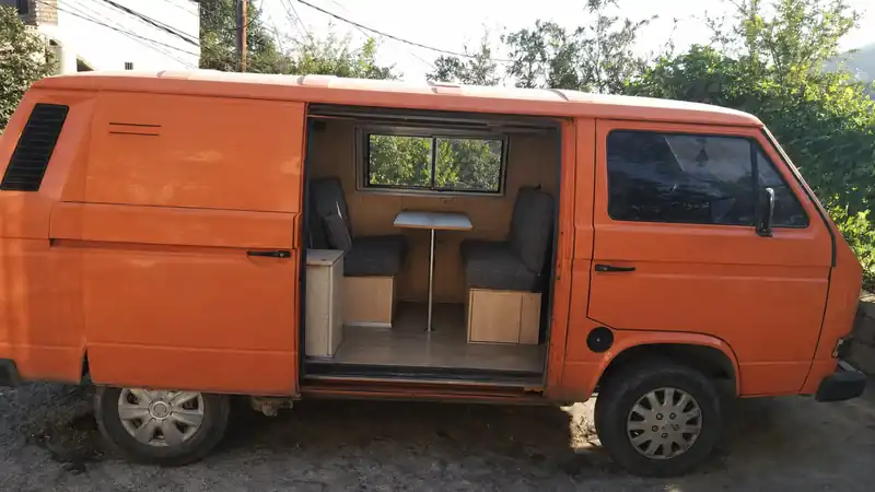 Orange camper van with the sliding door open showing a simple wooden interior