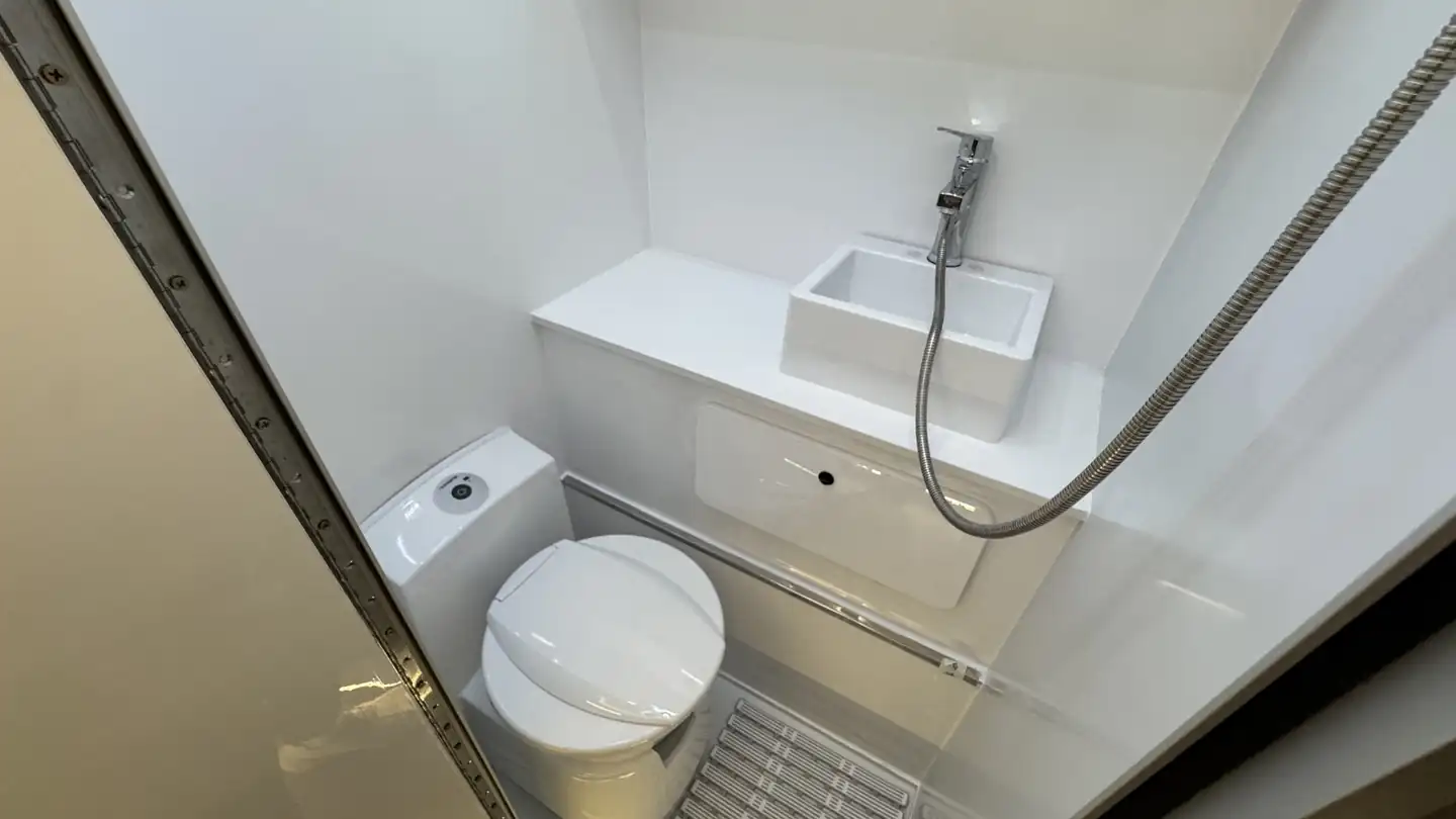 Compact camper bathroom with a cassette-style toilet, small sink and shower