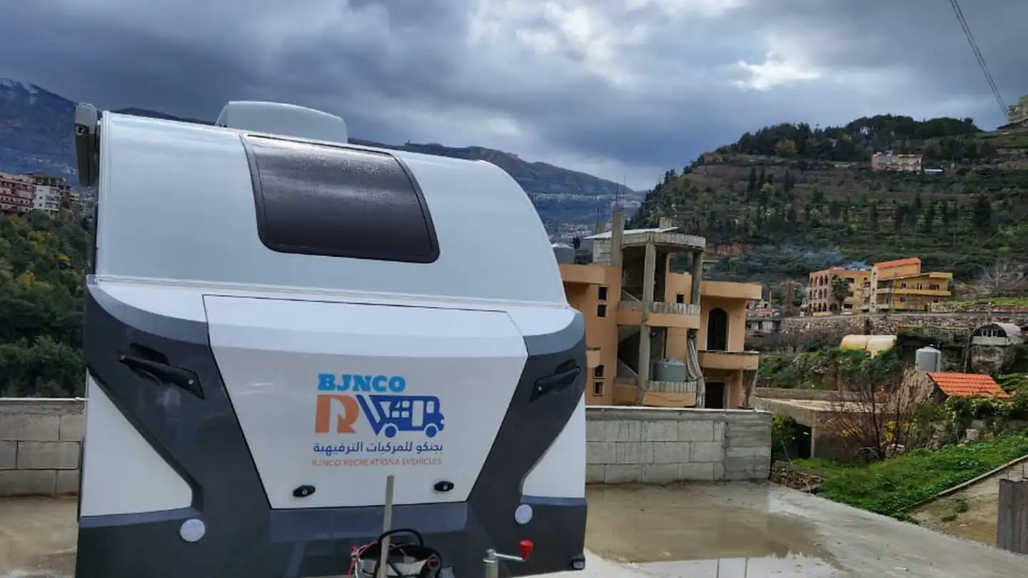 Touring caravan parked on a terrace with Lebanese mountain villages and clouds behind