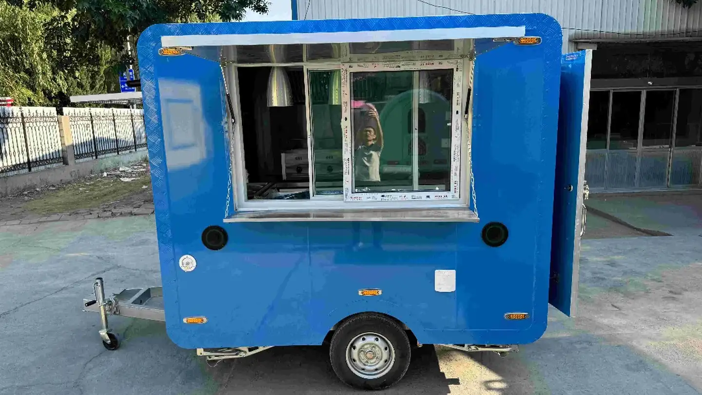 Blue food trailer with its serving hatch open, parked outside a workshop