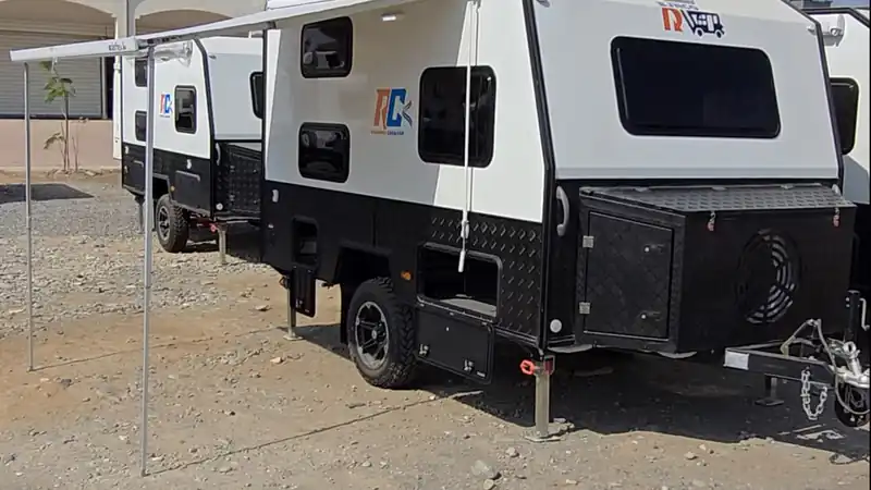 Off-road caravans with a deployed awning on a dry gravel lot under a clear sky