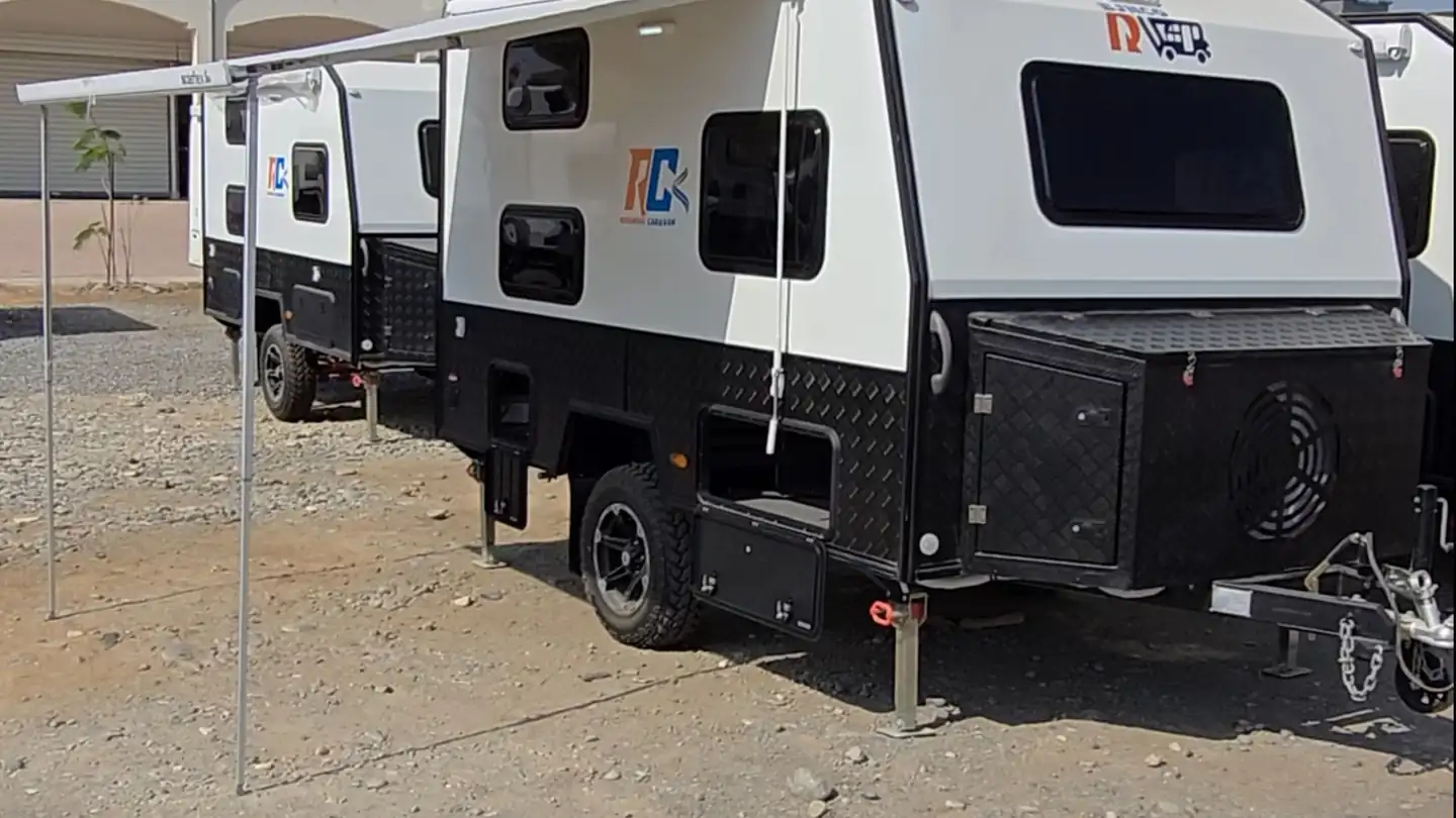 Off-road caravans with a deployed awning on a dry gravel lot under a clear sky