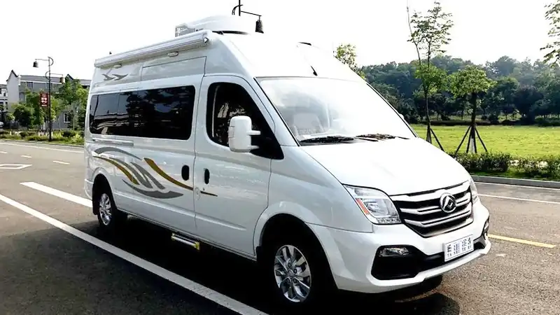 White high-roof Maxus campervan parked on a road beside green fields
