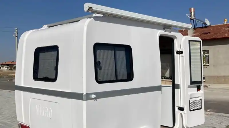 Compact rounded micro caravan with its side door open on a paved yard