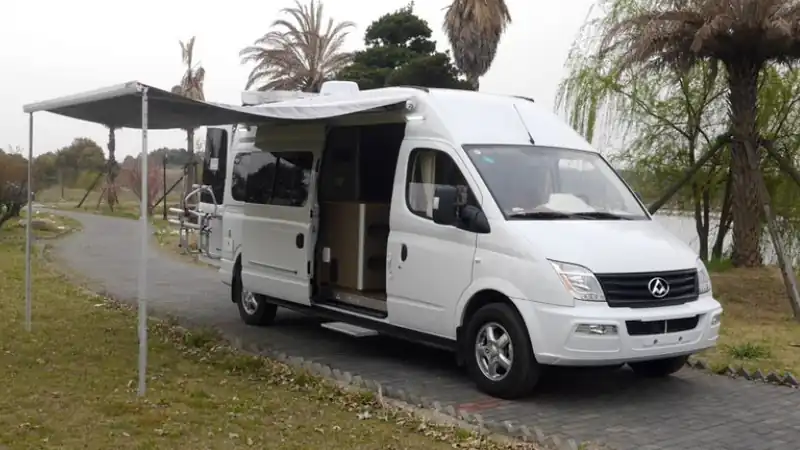 Campervan with its side door open and awning out, parked on grass under palm trees